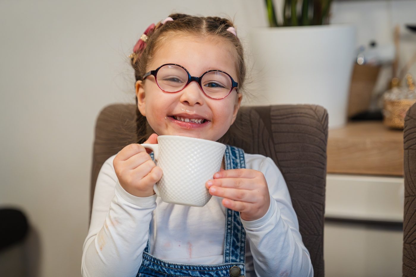 Une petite fille à lunettes sourit en tenant sa tasse