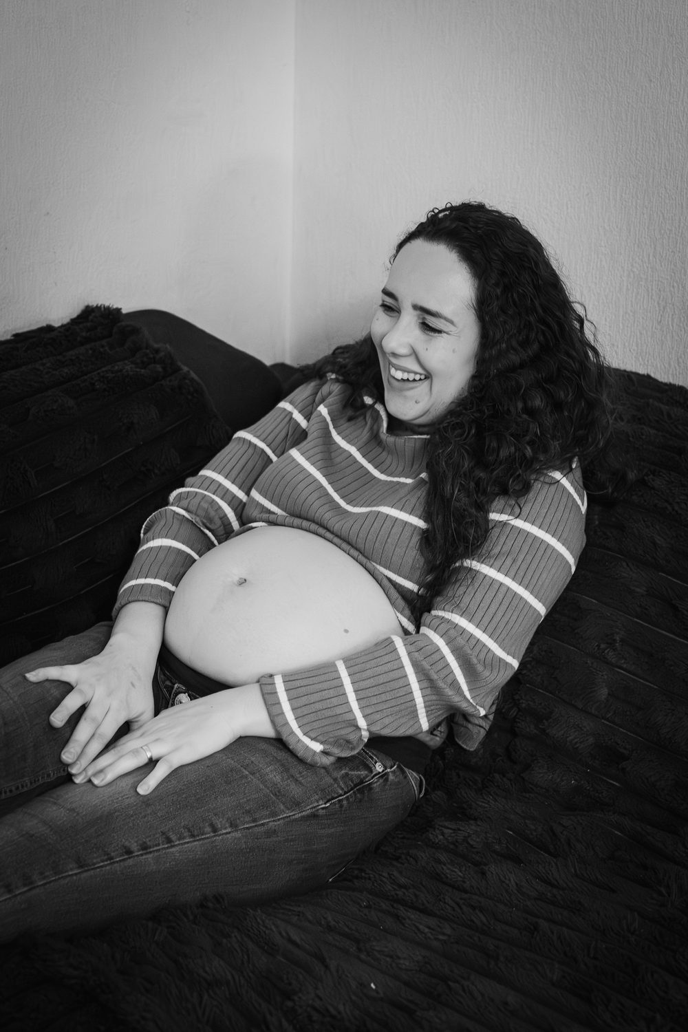Une femme enceinte rit sur son canapé, photo de grossesse en noir et blanc