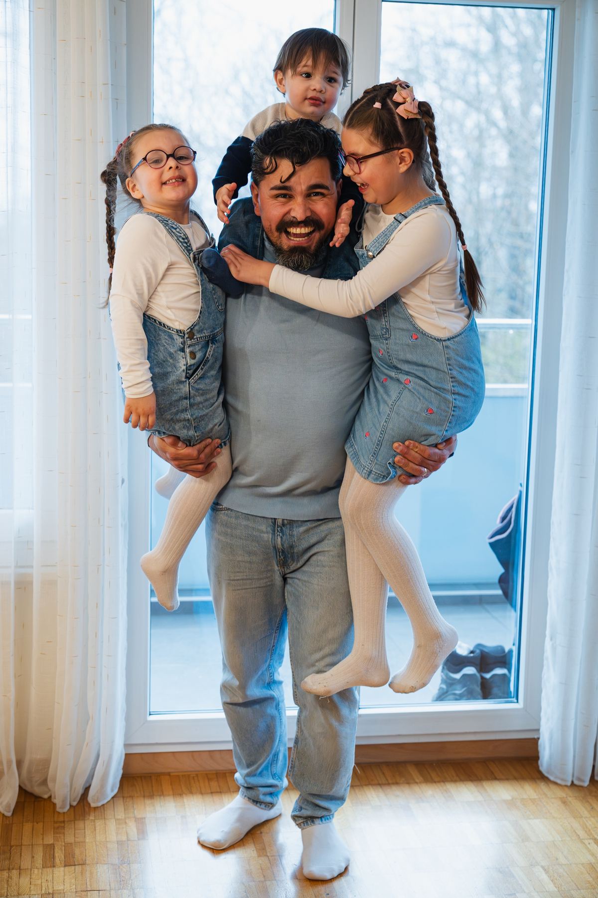Un papa porte ses deux filles dans ses bras et rit avec elles