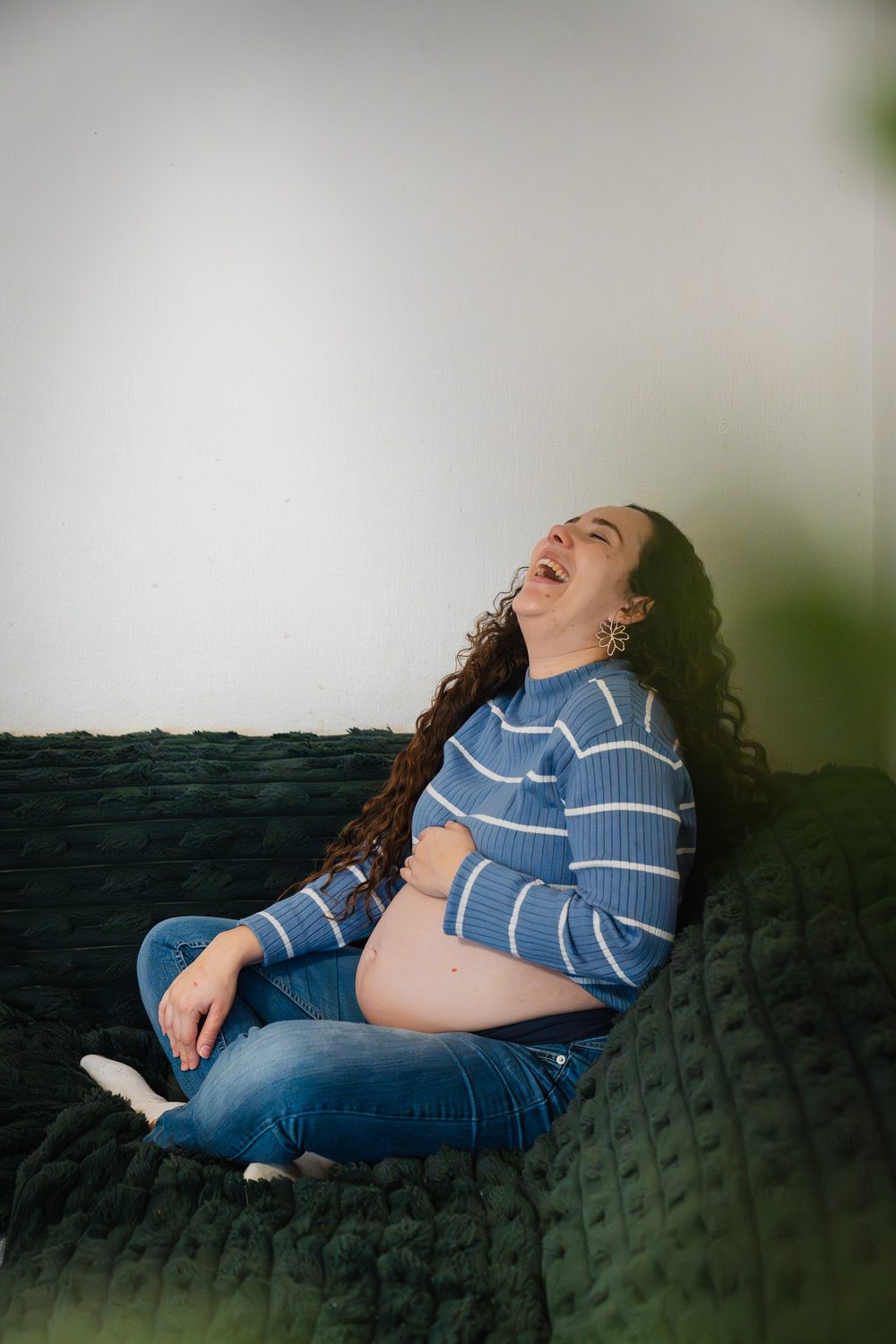 Une femme enceinte éclate de rire, allongée sur son canapé